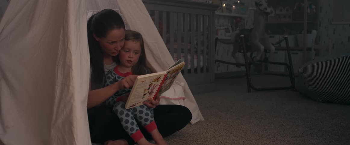 A woman sitting in a tent with her daughter on her lap reading a bedtime book in the nursery