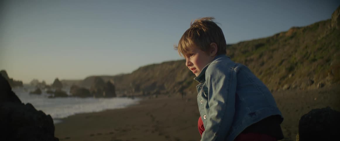 A child is sitting on the beach looking at the water