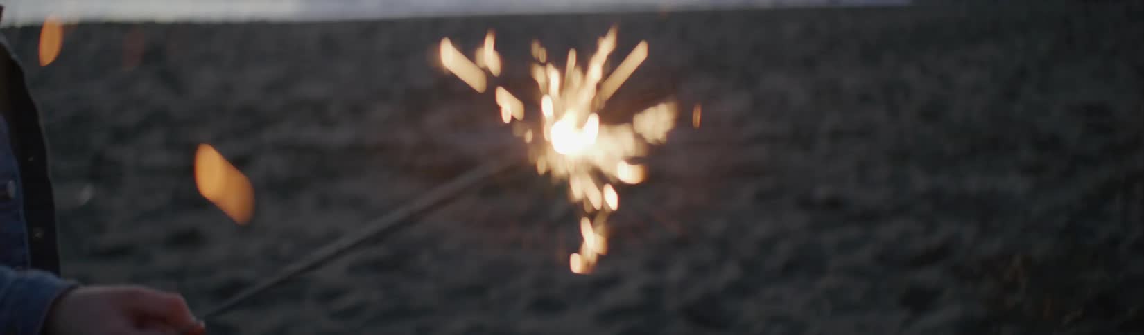 A child is holding a sparkler on the beach