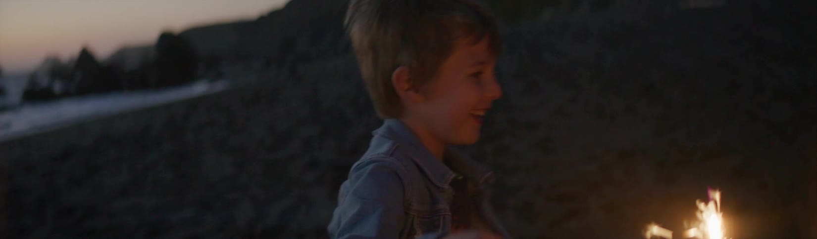 Happy boy holding a sparkler while running in the beach during sunset