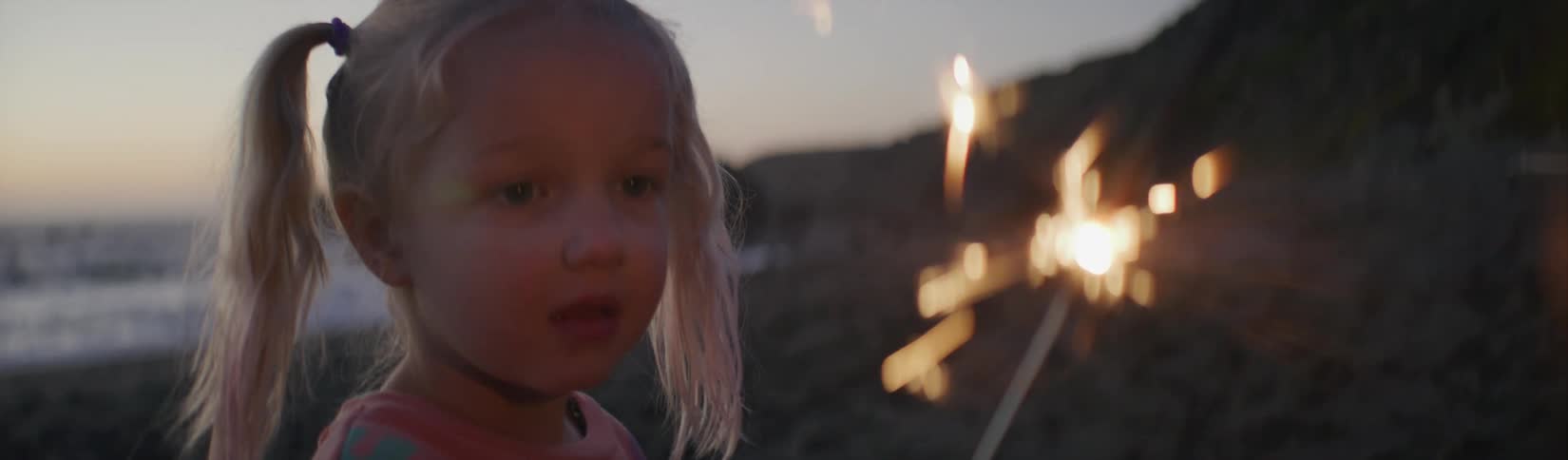 A girl is holding a sparkler on the beach