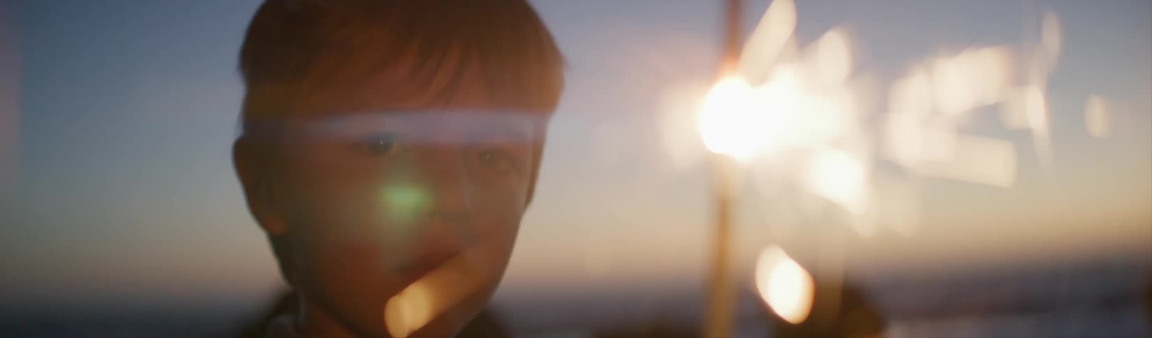 A young boy is on a beach holding a sparkler and watching the sparks fly