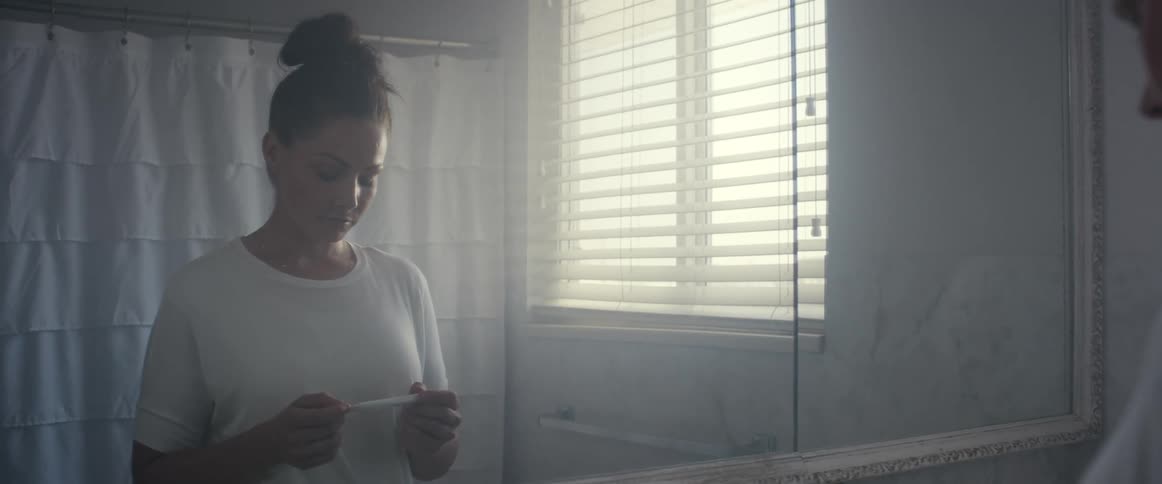 Woman standing in front of the mirror in the bathroom holding a pregnancy test
