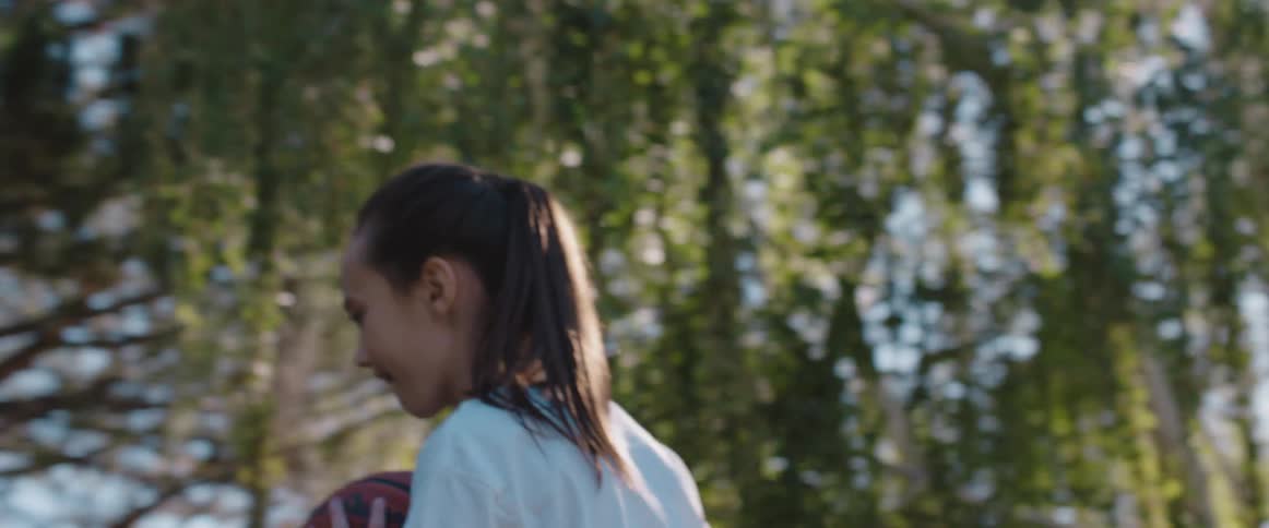 Young girl standing in front of the trees in the backyard throws a basketball at morning