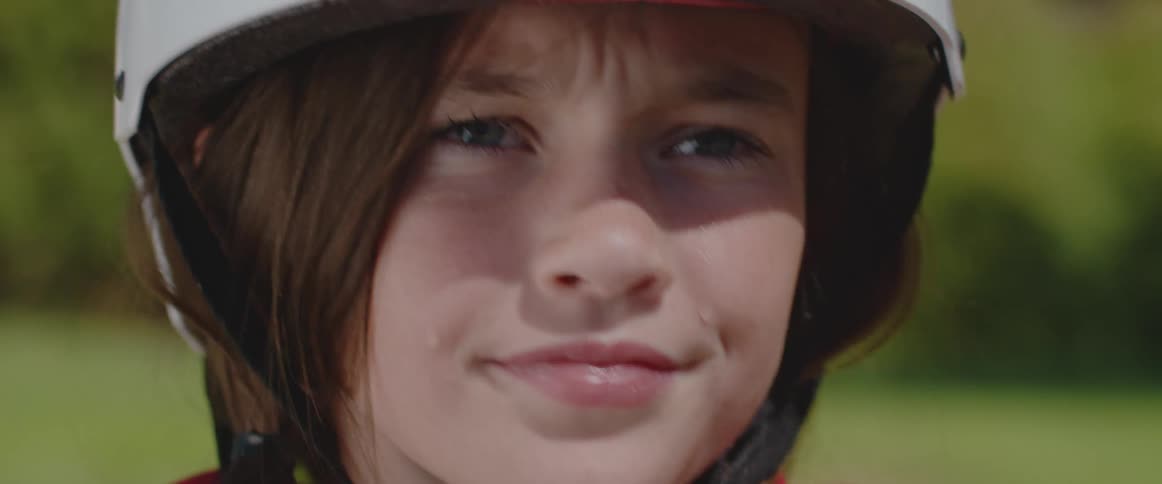 Young girl putting on a white safety helmet outdoors at a sunny day