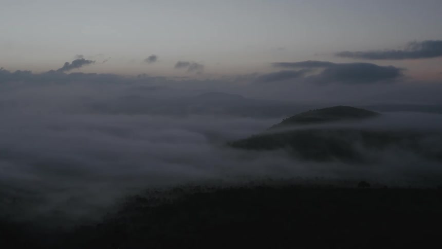 Low lying clouds move across the landscape under a red tinted sky obscuring the mountains