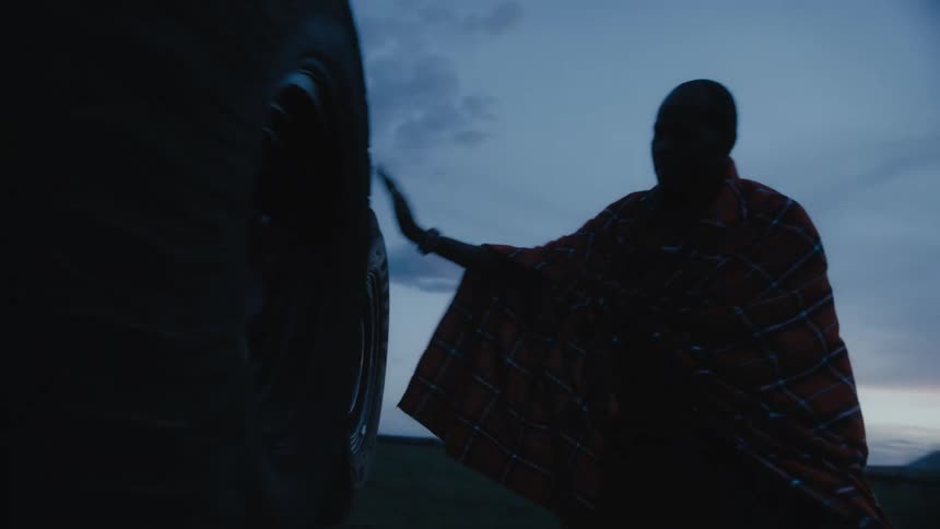 Black man walking around a car parked outdoors at an empty field