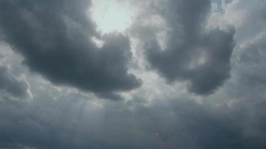 The sun shines behind dark clouds floating in the sky