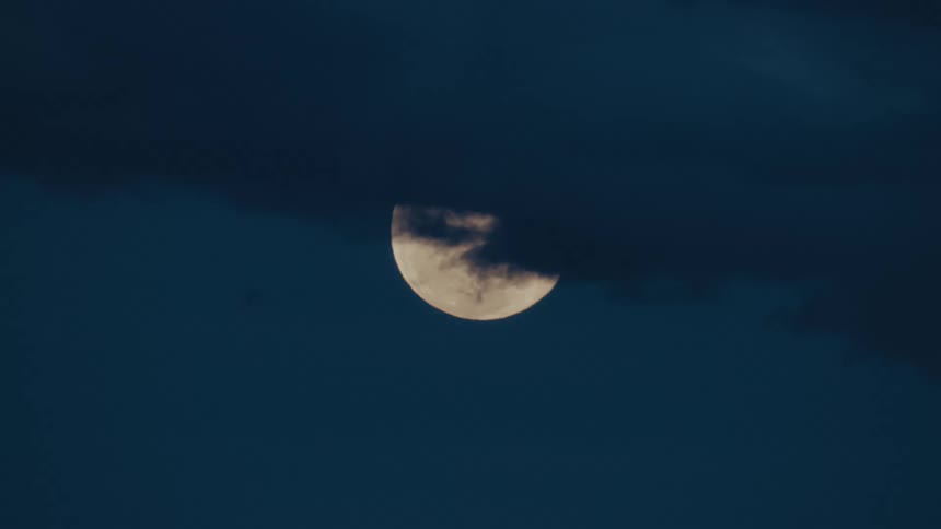 Clouds partially cover a full moon in the sky