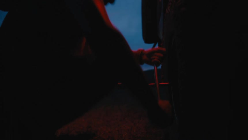 Black man using a lug wrench to change the tires of a car in the middle of an empty grass field during sunset