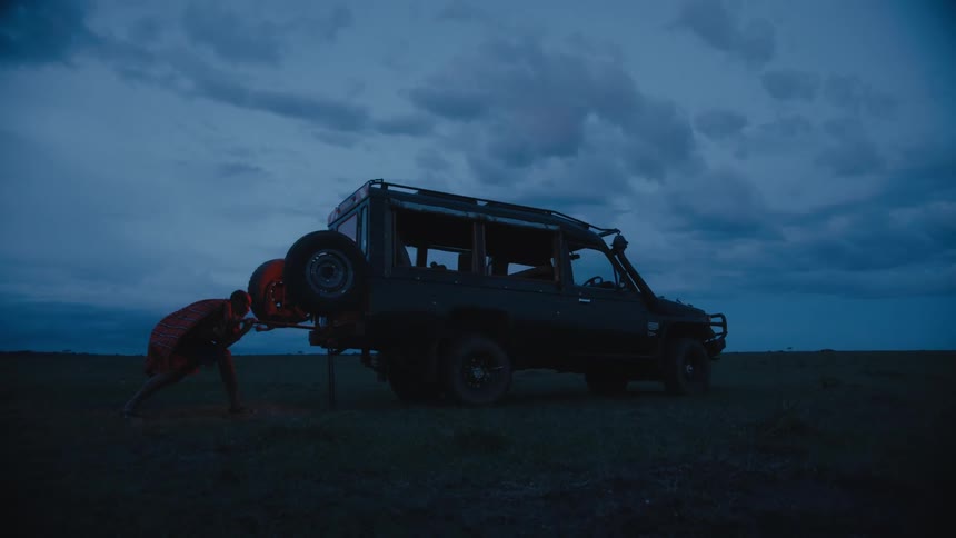 A man in traditional african garb uses a jack to lift a land rover