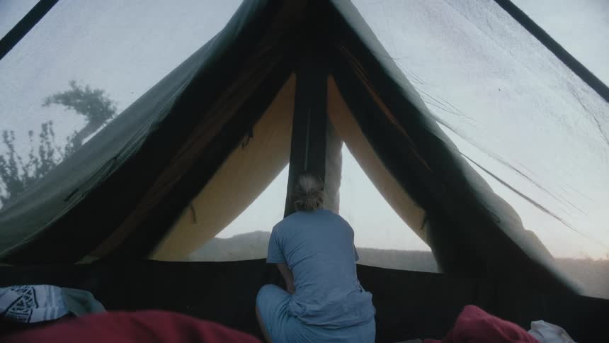 Woman crouches down and then rises as she unzips the opening to a tent