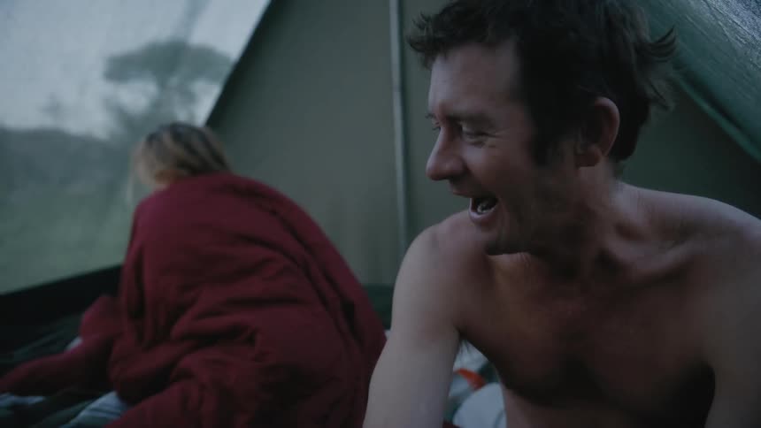 A man sitting up in a tent yawns as his wife and family wake up