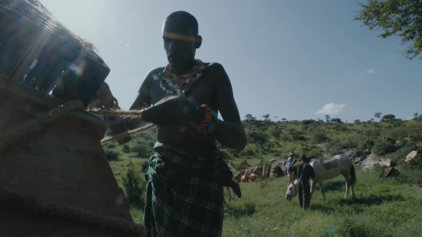 A man unwraps items in the back of a truck while other men groom horses in the background