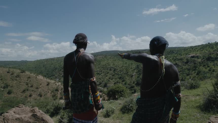 Two men talk and point towards the hills