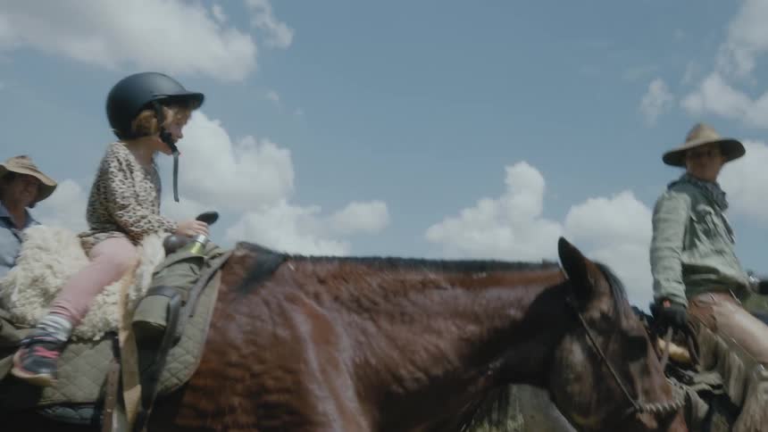 Little girl wearing a helmet riding a horse with her family outdoors