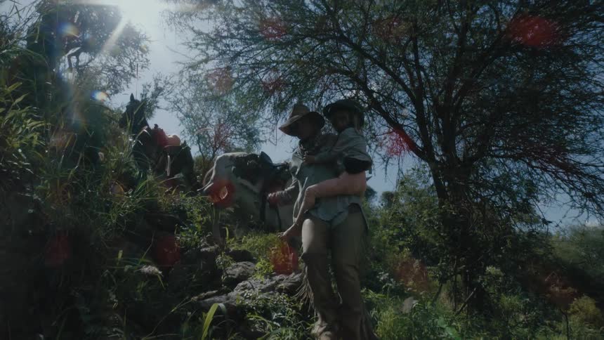 A man holds his daughter while trying to lead two horses down a rough hill