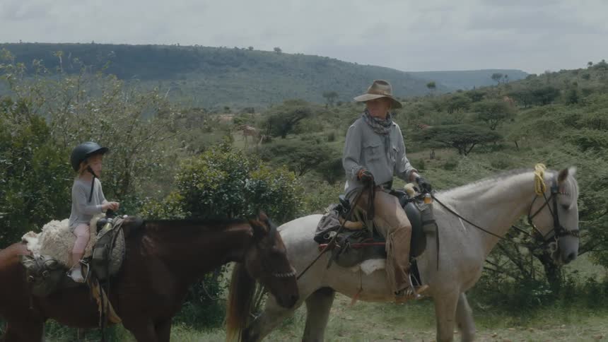 A man turns around to check on his daughter as she rides a horse behind his own