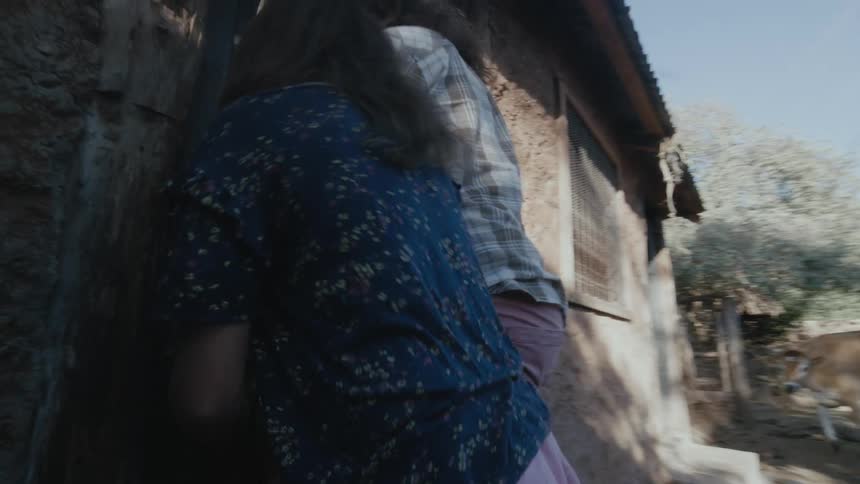 A woman opens the door to a small house for her daughter carrying a bundle of sticks