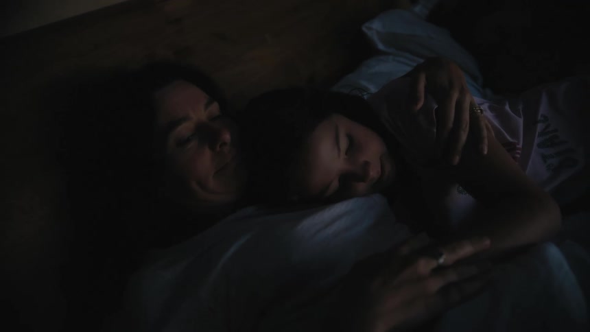 Mother and daughter snuggle together in bed as the daughter pushes the arm of her mother away