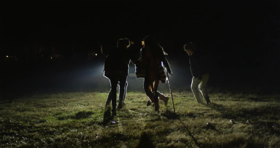 A group of people dancing in front of car headlights