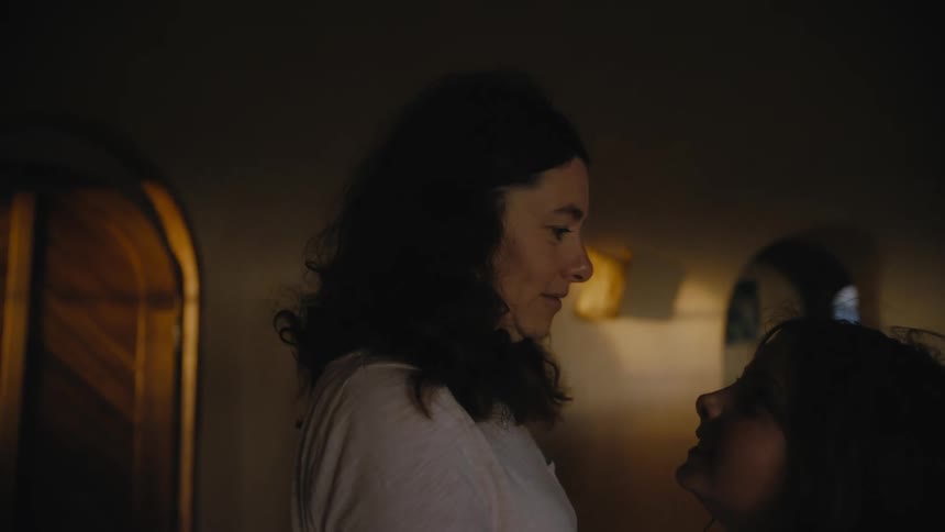 Mother with wavy hair and white shirt talks to daughter in room smiling at dusk