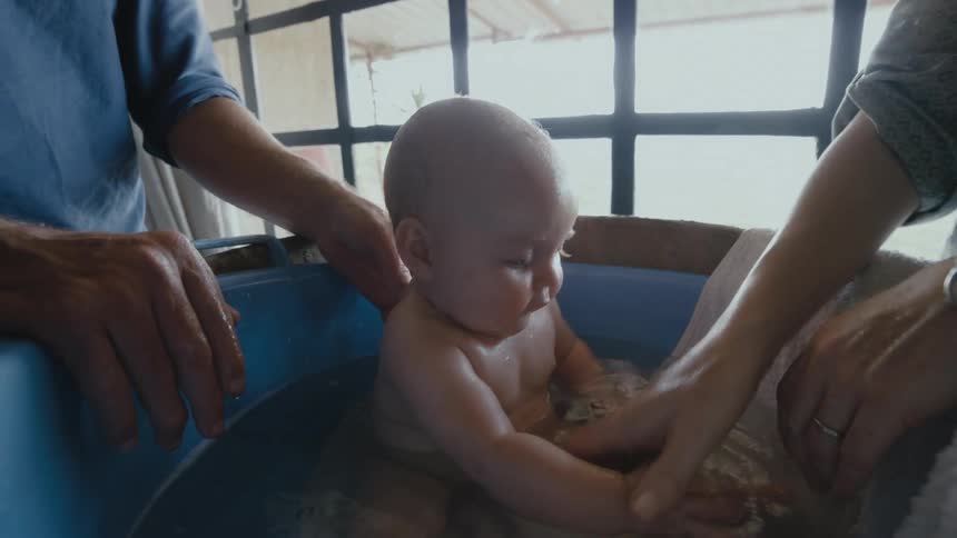 A man and woman stand over a young baby splashing in its bath water