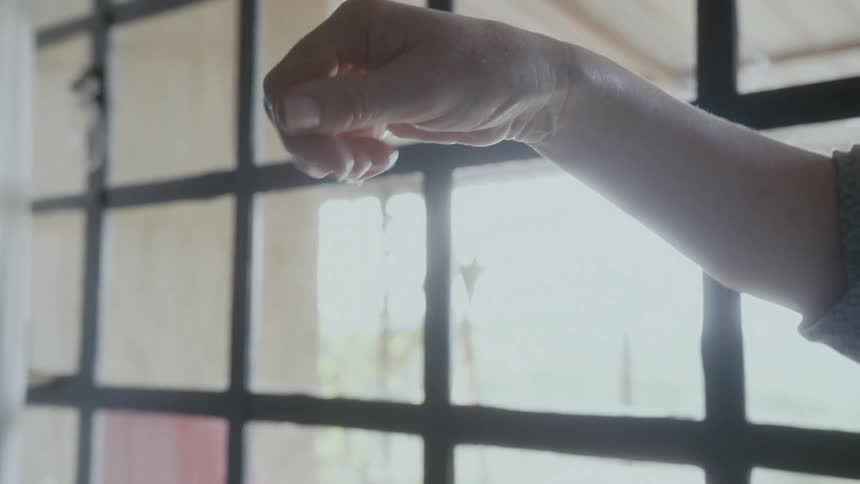 Mother playing with the water while bathing her baby in a plastic blue tub next to a big window