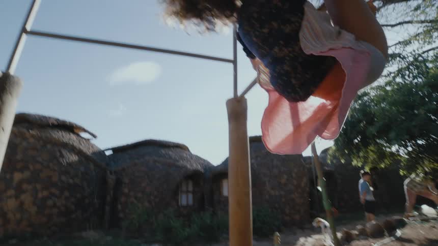 Happy girl playfully hangs upside down playing on monkey bars outdoors at morning