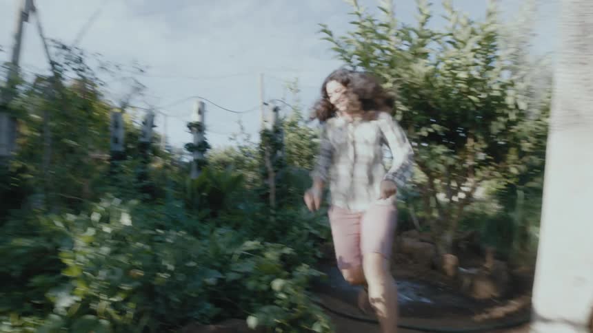 A mother chasing her young son in a garden on a sunny summer day