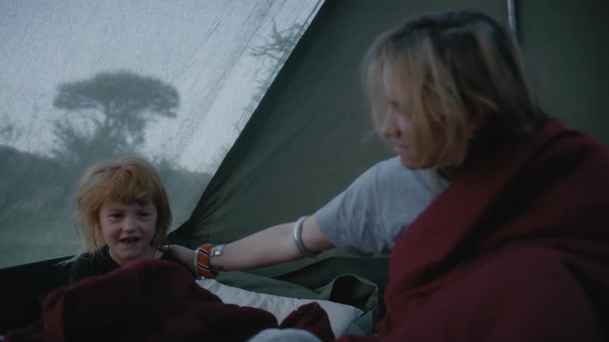 A mother in a tent rubs her daughters head as a young boy sits in his fathers lap