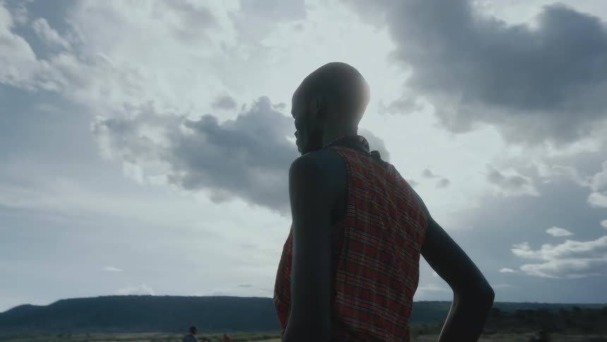 African man with traditional outfit stands and takes care of sheep and goat in the field