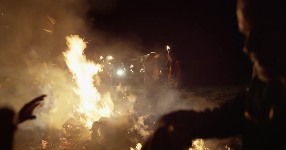 People are partying and waving sparklers by a campfire at night