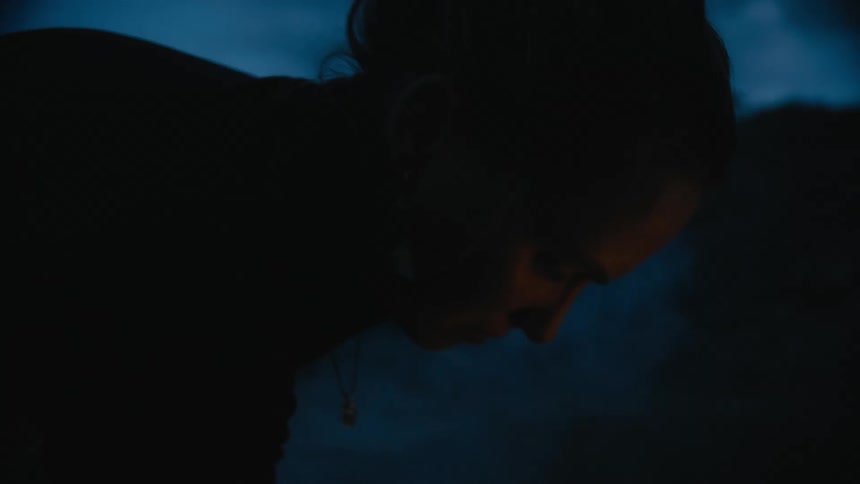 A woman is leaning over the smoke of the campfire