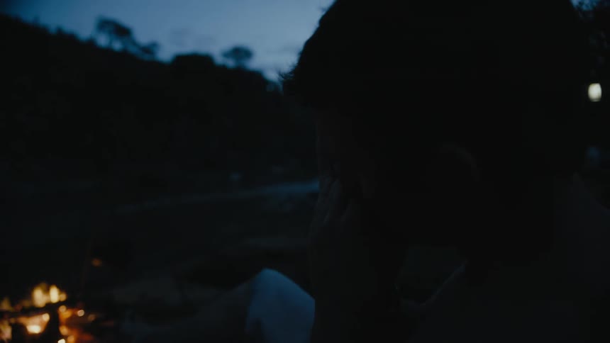 The silhouette of a man sitting by the camp fire playing a harmonica