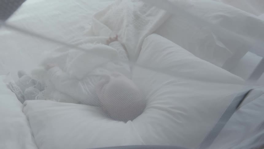 Baby lies in bed with white pillow and blanket