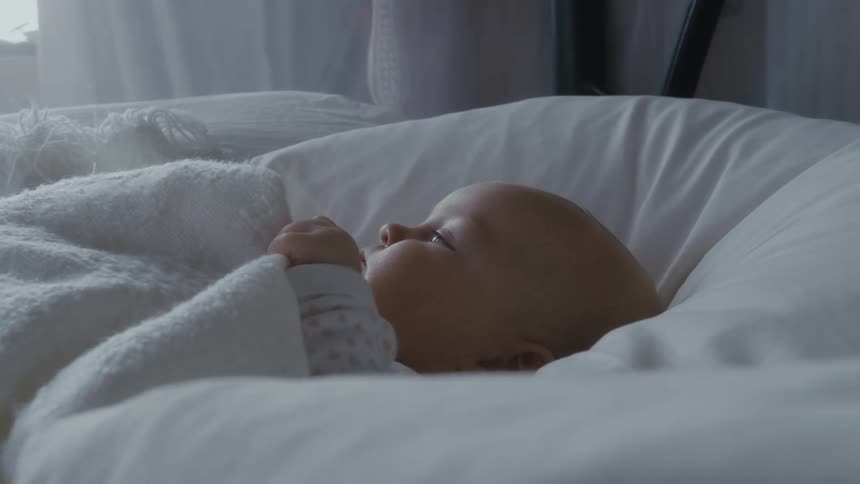 Baby lies in bed with white blanket and pillow