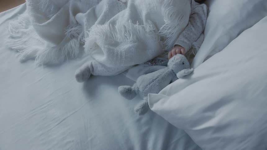A baby lying on a bed with a stuffed aimal and white blanket