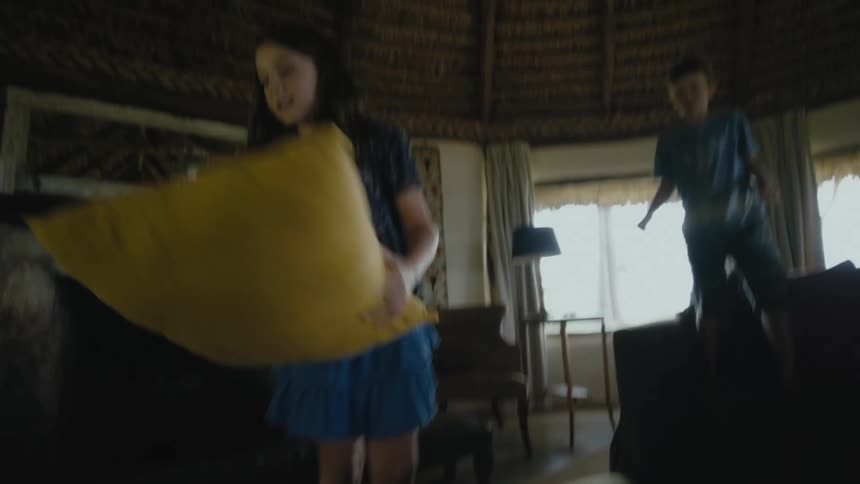 A boy throws a pillow to his sister while playing a game in their yurt