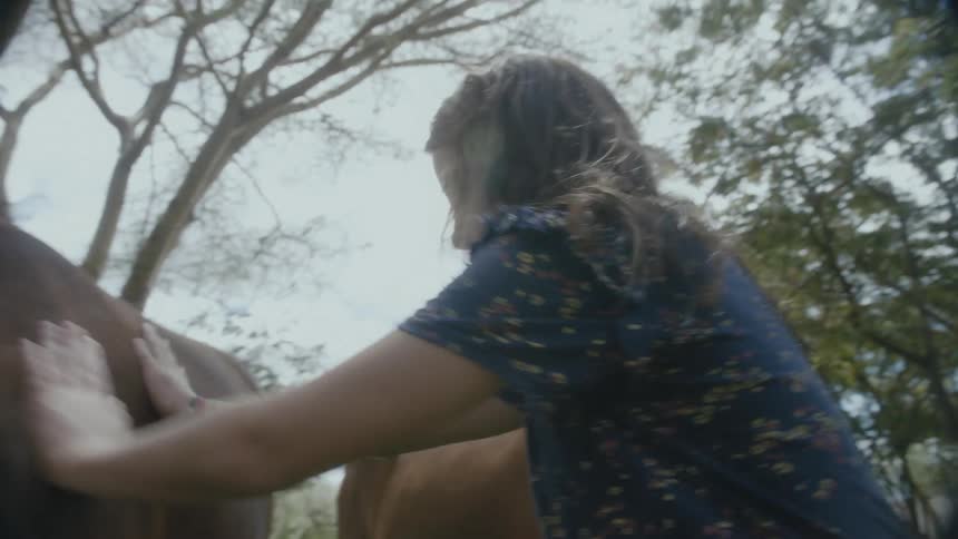 White girl petting a horse that is eating the grass at the grass field on a sunny day