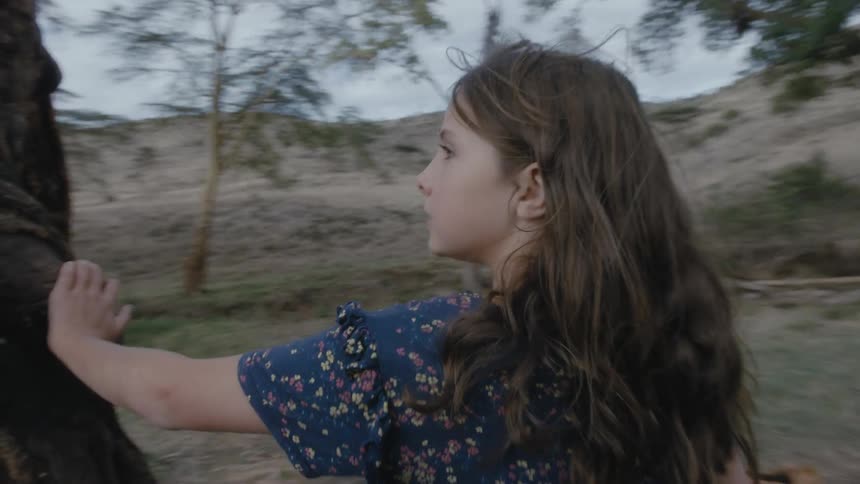 Teenaged girl sticks her finger into the side of a large tree then walks around to the other side of the tree