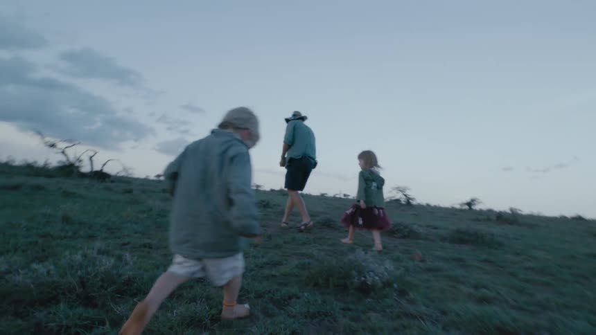 Father walks in a field with his son and daughter then he stops and crouches down