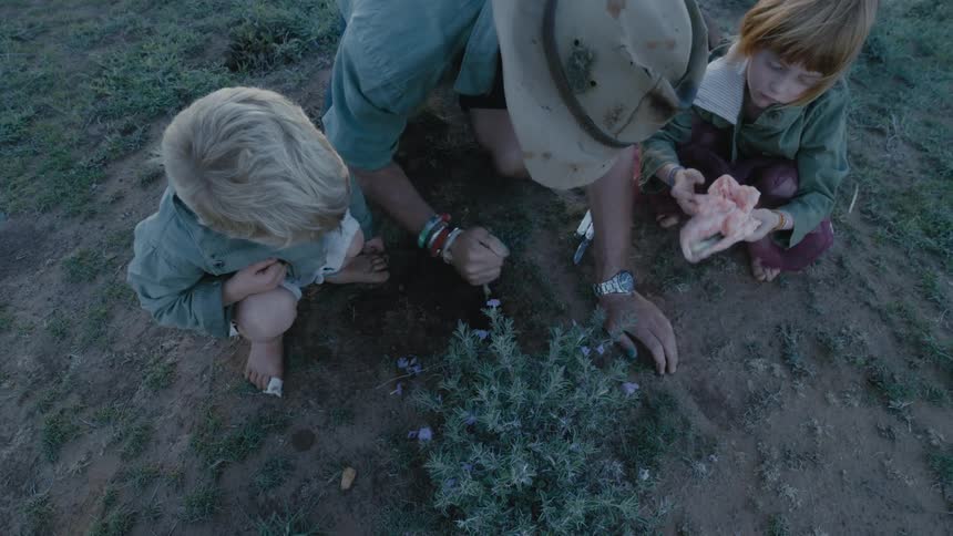 A man is digging in the ground as children watch