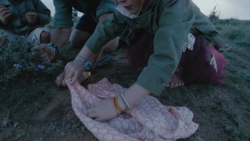 Young girl wrapping a dead bird in blanket as mother digs a hole