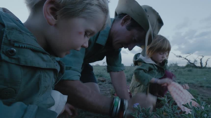 Dad digs a hole in the ground near flowers while his daughter wraps a dead bird up in a cloth