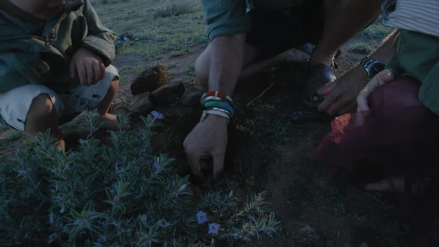 Father son and daughter burying a small dead bird into the ground in an open field