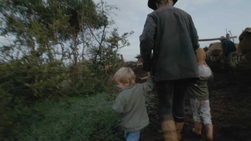 Woman holds the hands of a little boy and little girl as they walk towards the cows