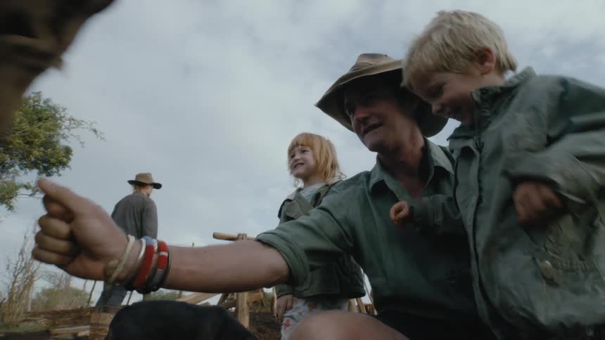A man shows his kids how to pet a cow on a farm