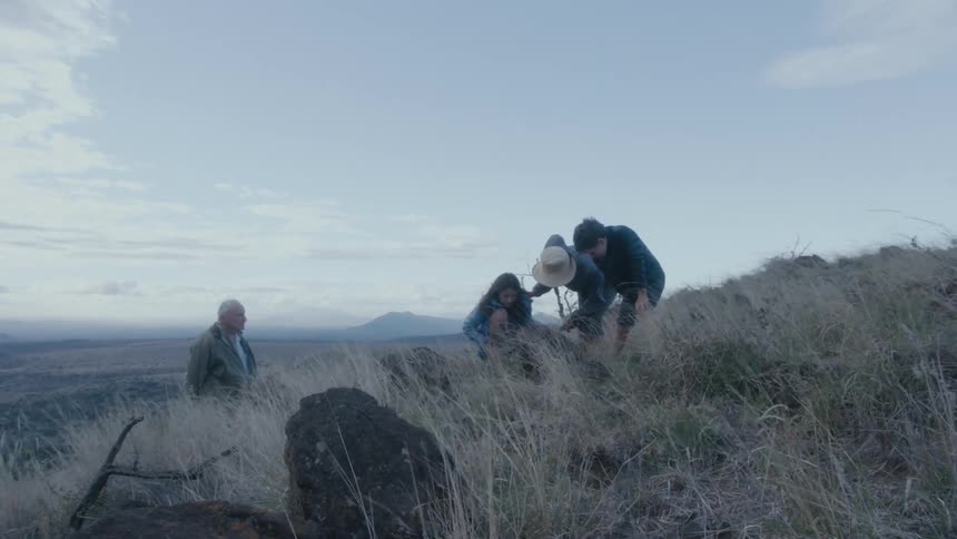 Grandparents and grandchildren pause in their hike over slope to explore ground