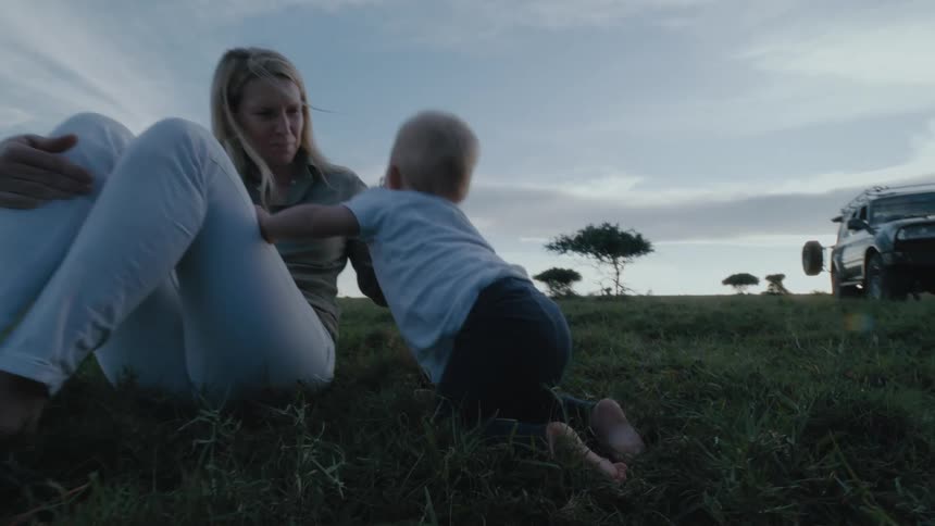 Baby crawls through the grass over to mom as the family relaxes near their land rover